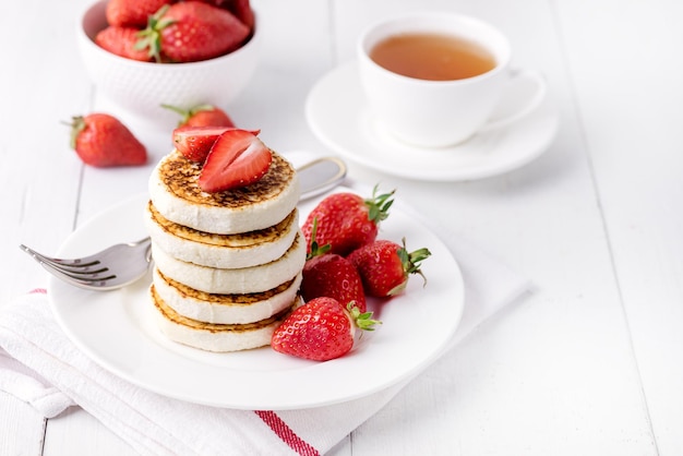 하얀 접시에 딸기를 곁들인 맛있는 수제 코티지 치즈 팬케이크