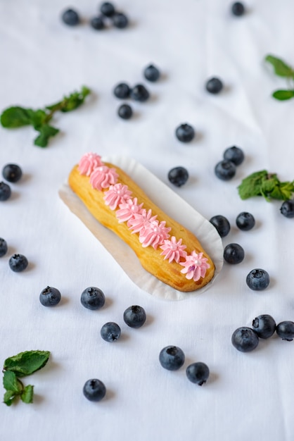 Tasty homemade eclairs on a white tablecloth. Blueberries are scattered everywhere.