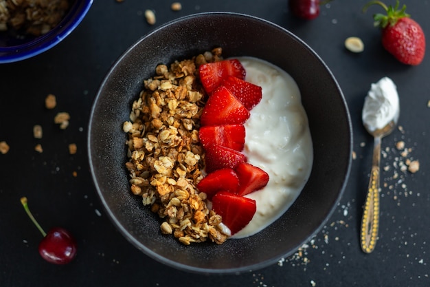Tasty homemade fruity muesli granola served in bowl with yogurt on dark background. closeup