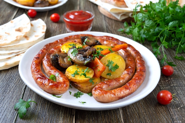 Tasty homemade grilled sausages with baked herb potatoes, mushrooms, cherry tomatoes and ketchup on a wooden background. Oktoberfest snack. Summer picnic dish