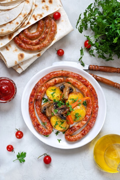 Gustose salsicce alla griglia fatte in casa con patate alle erbe al forno, funghi, pomodorini e ketchup su uno sfondo di legno. spuntino dell'oktoberfest. piatto da picnic estivo