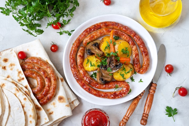 Tasty homemade grilled sausages with baked herb potatoes, mushrooms, cherry tomatoes and ketchup on a wooden background. Oktoberfest snack. Summer picnic dish