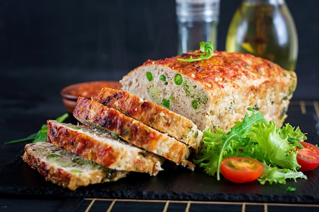 Tasty homemade ground  baked chicken meatloaf with green peas and broccoli on black table.