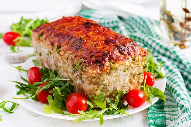 Tasty homemade ground baked chicken meatloaf with green peas and sliced broccoli on white table