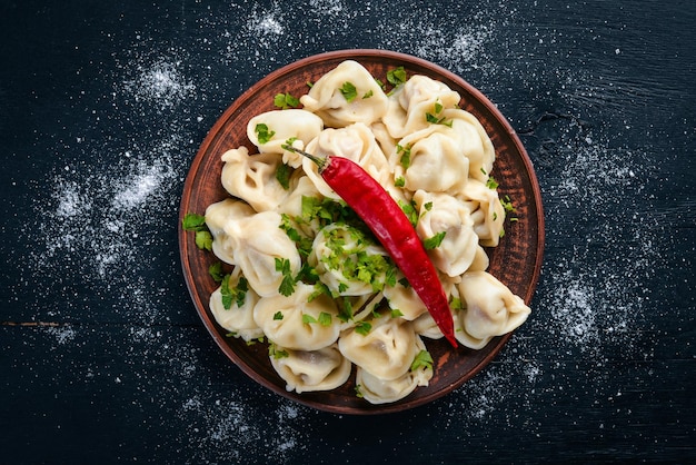 Tasty homemade meat dumplings of wholemeal flour or russian pelmeni sprinkled with fresh parsley on plate on wooden tablecopy space view from above