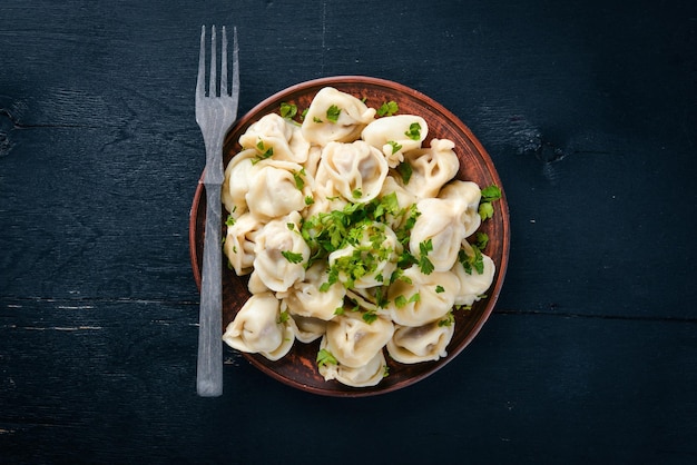 Tasty homemade meat dumplings of wholemeal flour or russian pelmeni sprinkled with fresh parsley on plate on wooden tablecopy space view from above