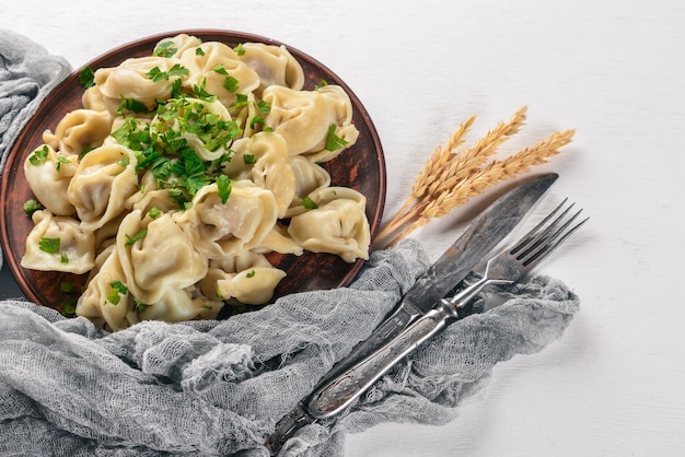 Photo tasty homemade meat dumplings of wholemeal flour or russian pelmeni sprinkled with fresh parsley on plate on wooden tablecopy space view from above