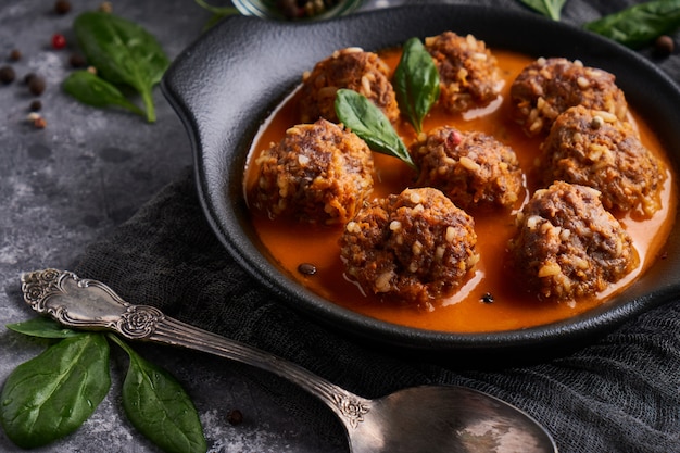 Le polpette fatte in casa saporite con salsa al pomodoro e gli spinaci sono servito in un piatto su una tavola di pietra scura chiuda su