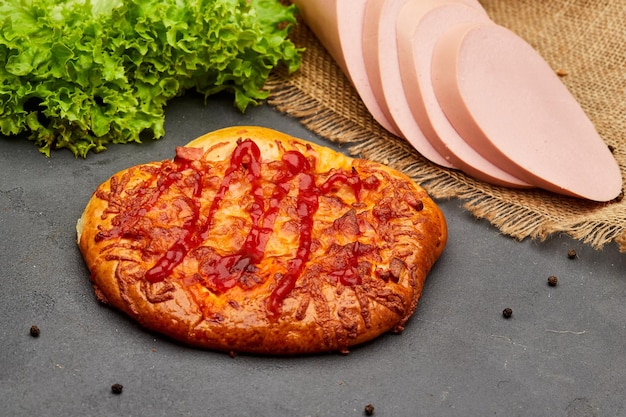 소시지와 치즈를 곁들인 맛있는 홈메이드 피자는 어두운 석재 배경에 제공됩니다. 건강에 해로운 음식