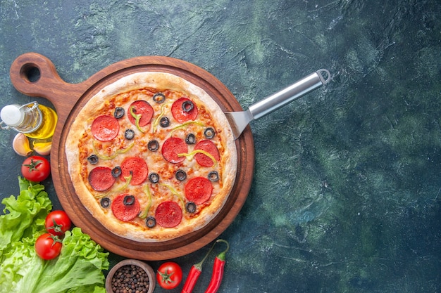 Tasty homemade pizza on wooden board oil bottle tomatoes pepper green bundle on the right side on dark surface