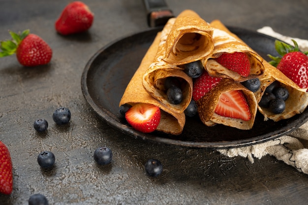 Tasty homemade rustic pancake with berries in a frying pan on wooden table. Maslenitsa food.