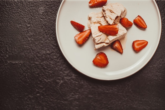 Tasty homemade vanilla ice cream with strawberry on a white plate on a dark background. Summer and sweet menu concept.