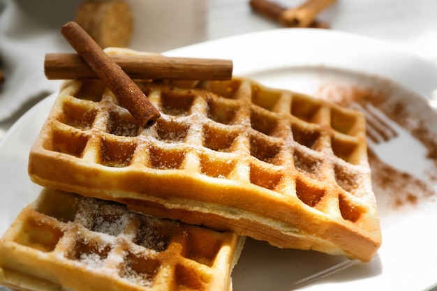 Tasty homemade waffles with sugar powder and cinnamon sticks, closeup