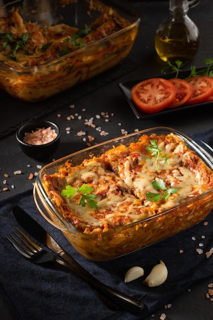 Tasty hot lasagna served on black background with ingredients around