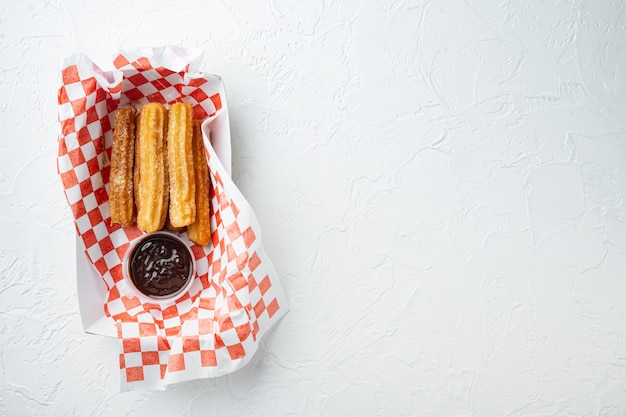 Tasty hot sweet churros in paper with chocolate, and caramel  in paper tray, on white background, top view flat lay with space for text, copyspace