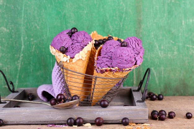 Tasty ice cream with berries in waffle cones on green wooden background