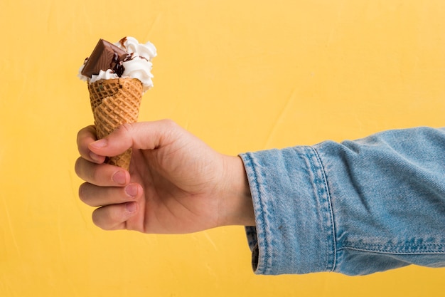 Вкусное мороженое с шоколадом и сиропом в конусе в руке