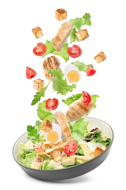 Tasty ingredients for Caesar salad falling into plate on white background