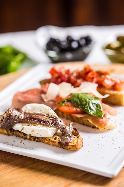 Tasty italian appetizer bruschettes with tomatoes anchovies prosciutto and mozarella.