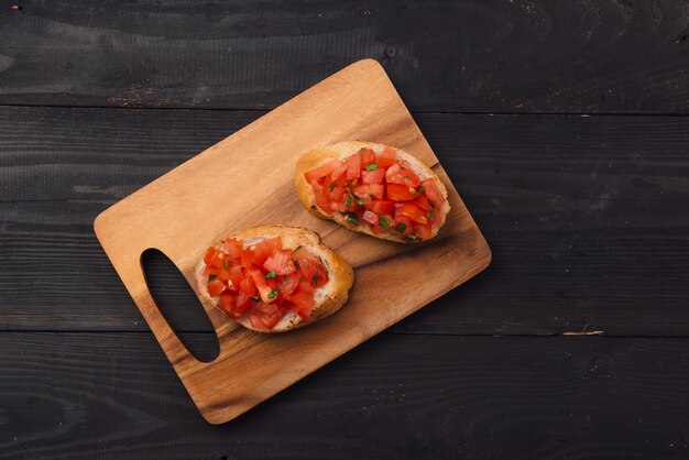 Tasty Italian bruschetta with  bread topped with tomato and herbs on wooden board