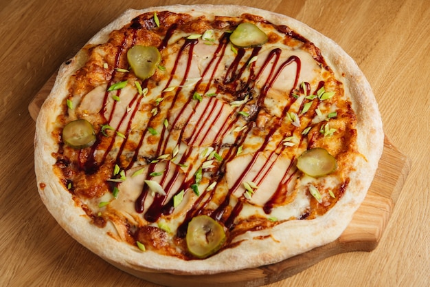 Tasty italian pizza with meat, pickles and sauce on wooden board