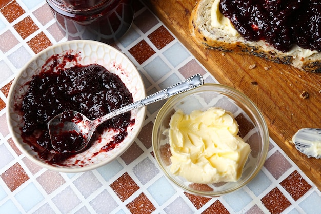 Photo tasty jam on the plate butter fresh bread and wooden tablet on mosaic background