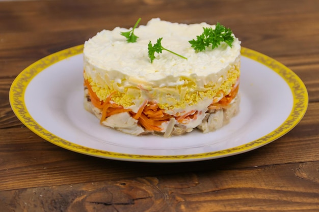 Tasty layered salad with chicken, carrot, eggs, cheese and mayonnaise on wooden table