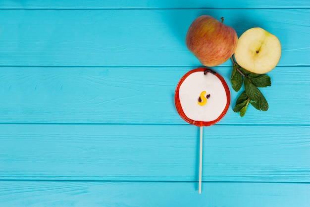 Tasty lollipop as an apple on wooden turquoise board near delicious sliced apple and a sprig of mint