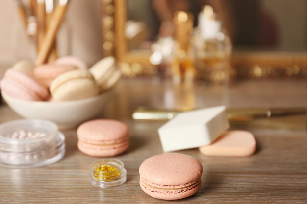 Tasty macaroons and beauty accessories on table