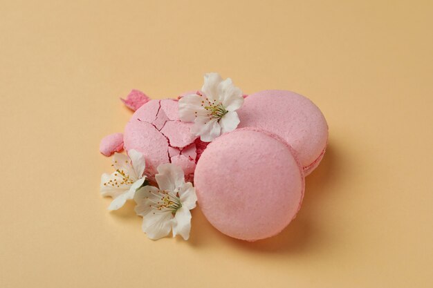 Tasty macaroons and flowers on beige background