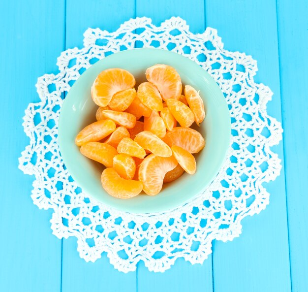 Ломтики вкусного мандарина на цветной тарелке на синей поверхности