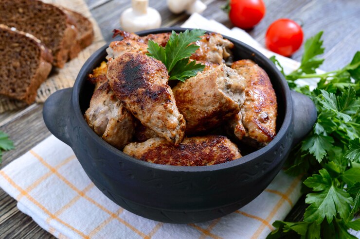 Вкусные мясные рулетики с грибами в керамическом горшке на деревянном столе