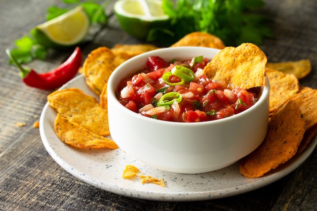 Tasty mexican nachos chips in bowl with salsa dip on wooden table