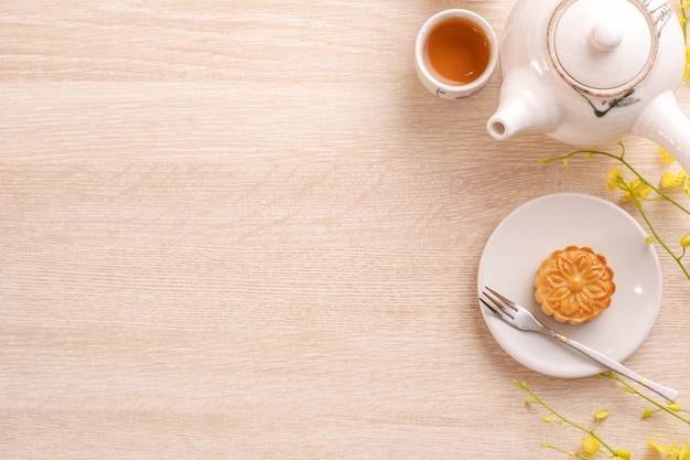 Tasty moon cake for Mid-Autumn festival on bright wooden table, concept of festive afternoon tea decorated with yellow flowers, top view, flat lay