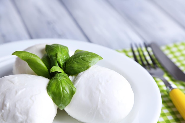 Tasty mozzarella cheese with basil on plate on wooden background