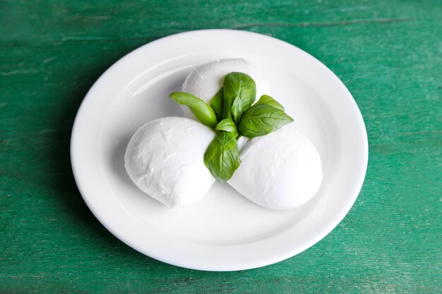 Tasty mozzarella cheese with basil on plate on wooden background