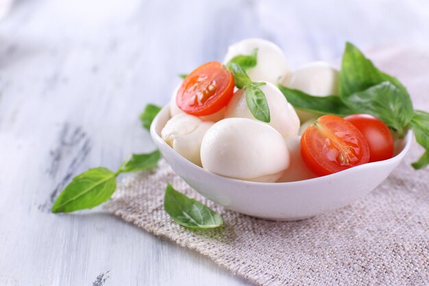 Tasty mozzarella cheese with basil and tomatoes in bowl on wooden table