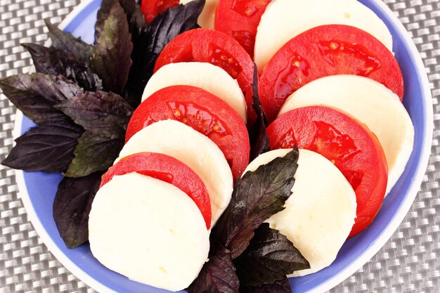 Tasty mozzarella with tomatoes on plate on mat