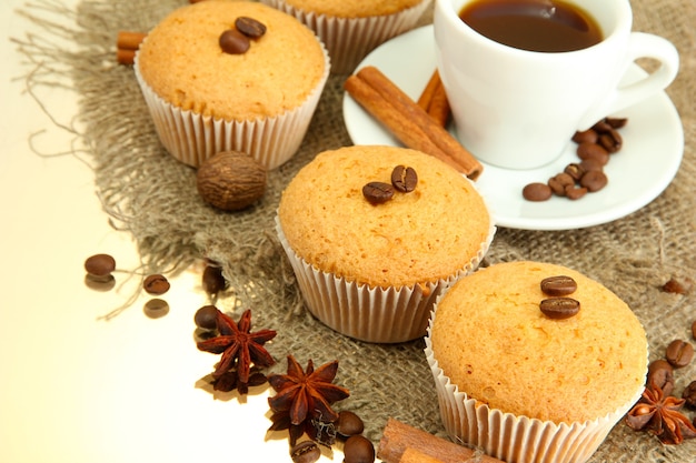Tasty muffin cakes with spices on burlap and cup of coffee, on beige background