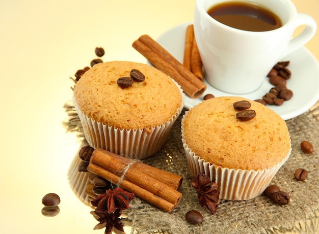 Tasty muffin cakes with spices on burlap and cup of coffee, on beige background