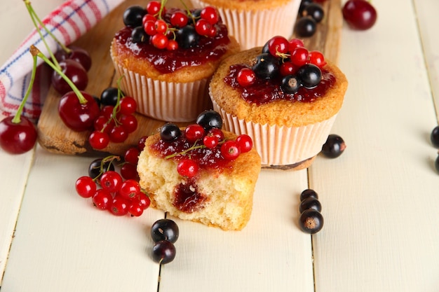 Tasty muffins with berries on white wooden table