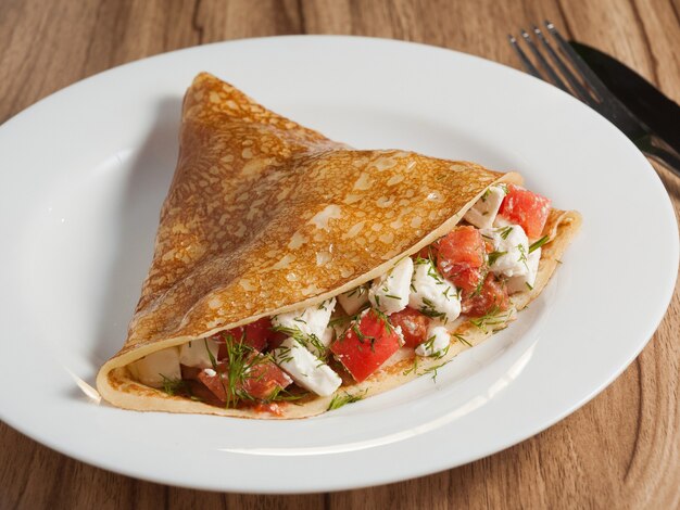 Tasty pancake with cheese and tomatoes on a white plate