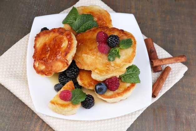 Tasty pancakes with fresh berries honey and mint leaf on plate on wooden background