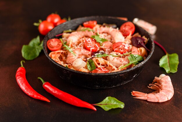 Tasty pasta with shrimp and tomato on a frying pan