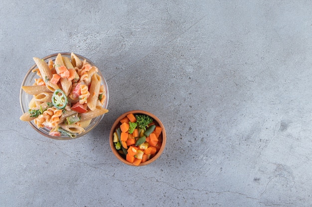 Tasty penne pasta and fresh salad on stone background. 