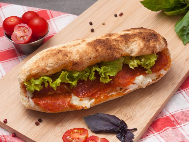 Tasty pepperoni panini with cream cheese and salad on a wooden board