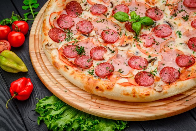 Tasty pepperoni pizza and cooking ingredients tomatoes basil on black concrete background Top view of hot pepperoni pizza With copy space for text Flat lay