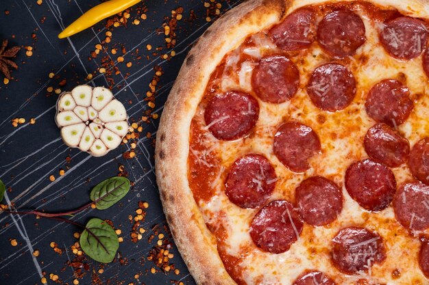 Tasty pepperoni pizza and cooking ingredients tomatoes basil on black concrete background