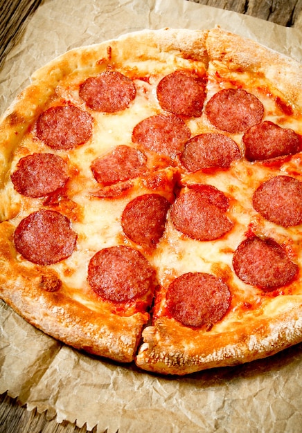 Tasty pepperoni pizza on an old paper. On a wooden background.