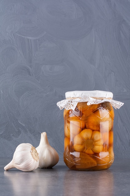 Tasty pickled garlic in glass jar placed on stone table.